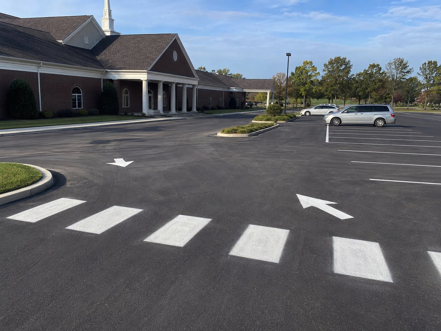 White crosswalk markings and directional arrows freshly painted at church parking lot in North Alabama — brick church building with steeple visible in background
