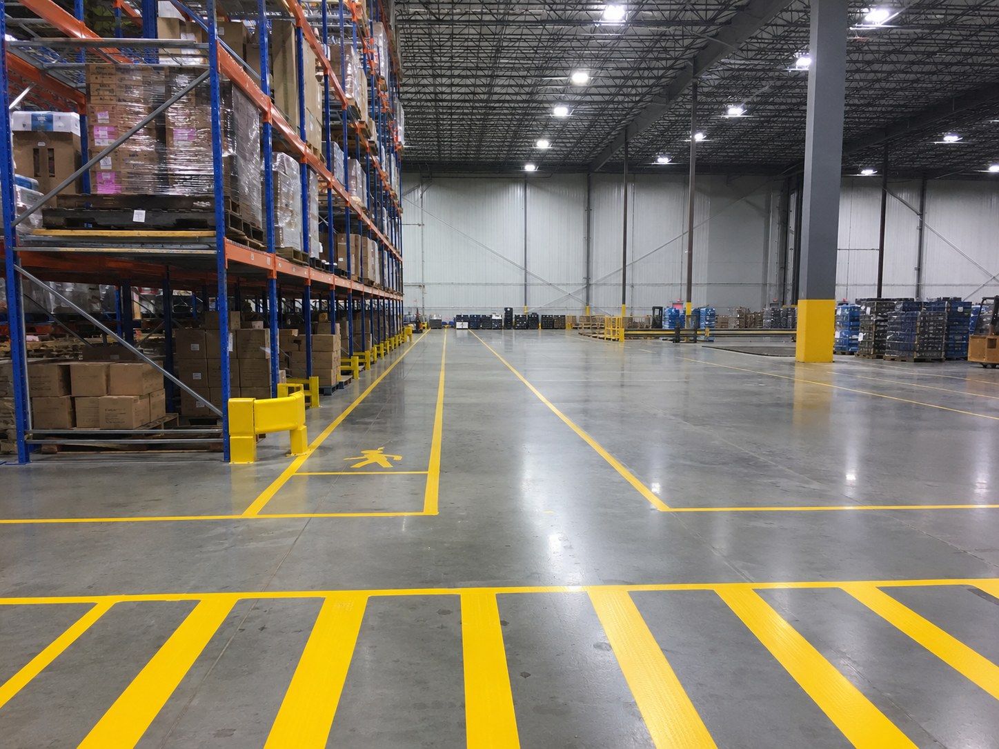 Yellow epoxy safety lines and pedestrian pathway markings on concrete warehouse floor — forklift travel lanes and pedestrian walkways clearly marked in large Huntsville distribution facility